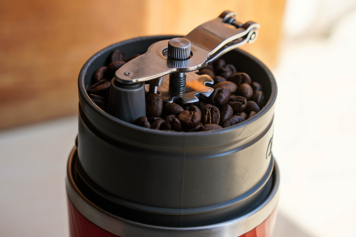 Moedor de café elétrico em aço inox sobre a bancada com xícara ao lado.
